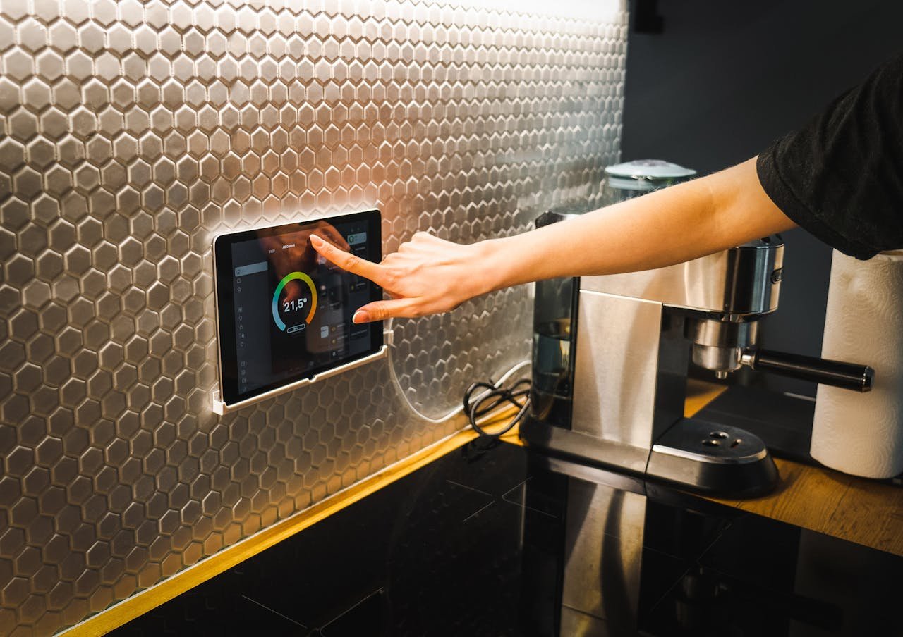 Modern kitchen scene featuring a hand using a tablet to control a smart home system.